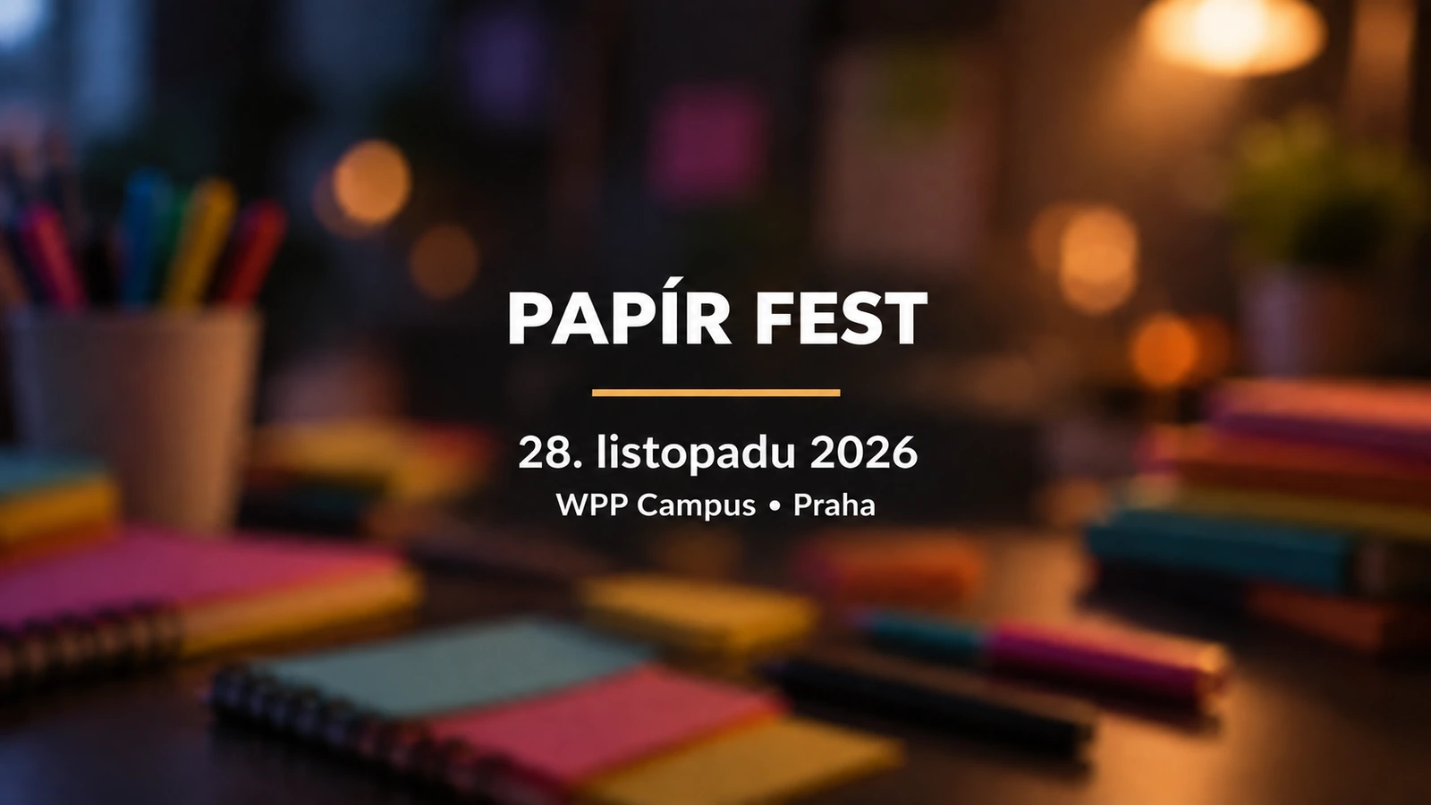 Papír Fest: bílý název a zlatá linka na rozostřeném pozadí zápisníků a psacích potřeb