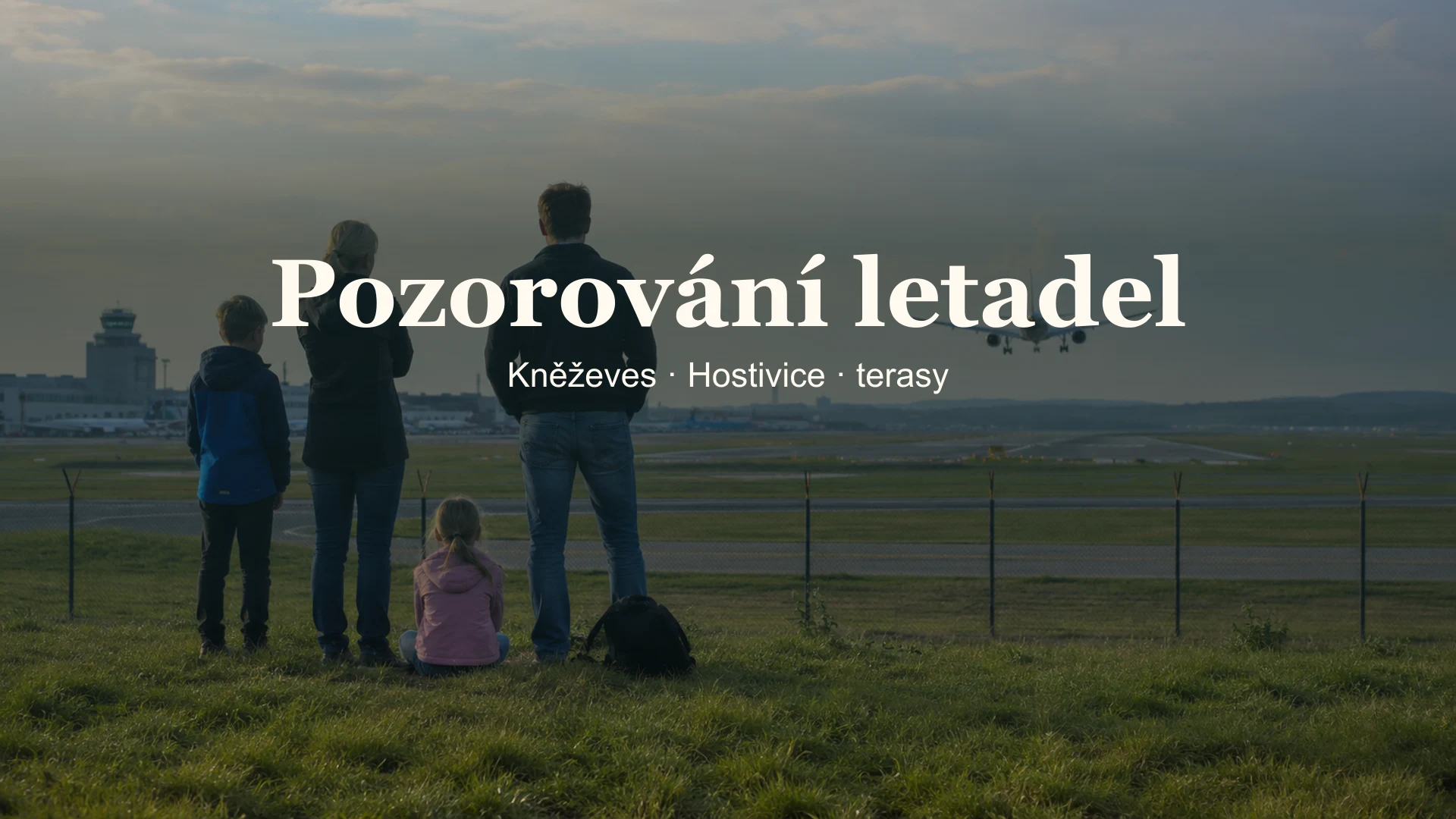Rodina sleduje přistávající letadlo z veřejného pozorovacího místa.